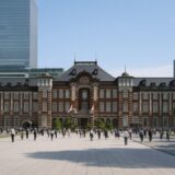 晴天の下、赤レンガ造りの東京駅丸の内駅舎を背景に、多くの人々が行き交う駅前広場の様子。高層ビル群と調和する都市の活気が感じられるシーン